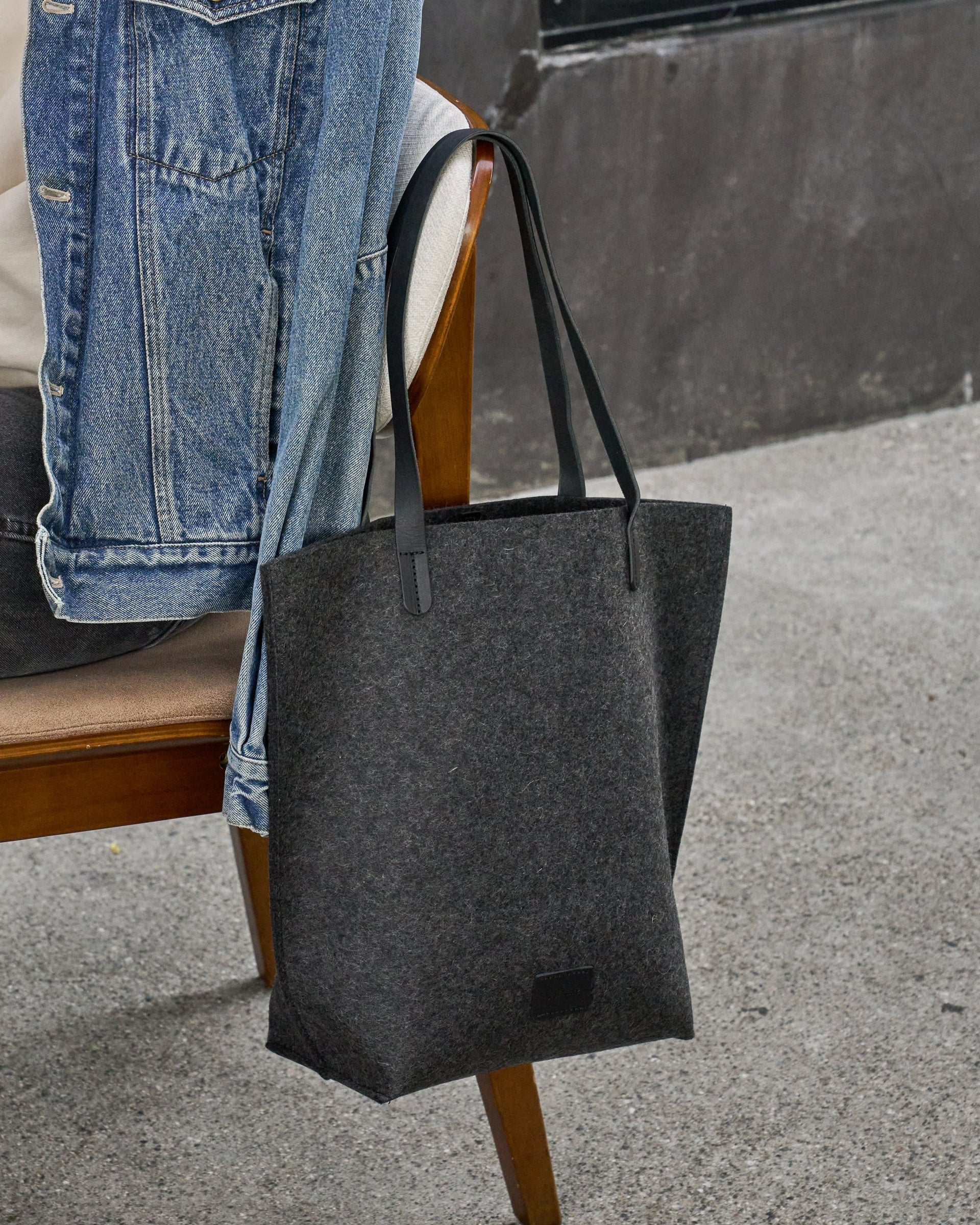 A charcoal-colored Hana Merino Wool Felt Tote hanging over chair back
