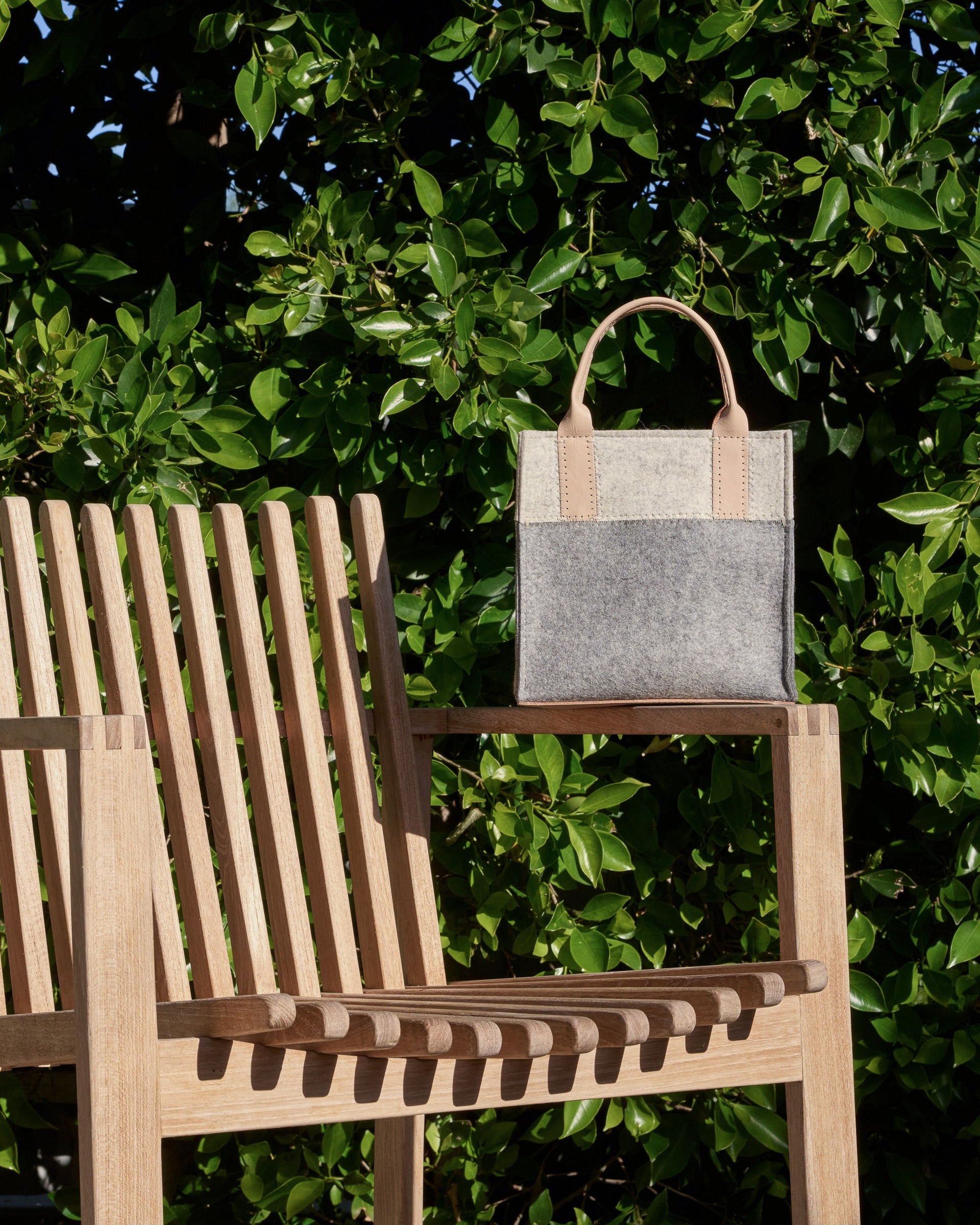 Grey, white, and beige crossbody Jaunt Mini Merino Wool Felt Tote resting on the arm of a wooden garden chair