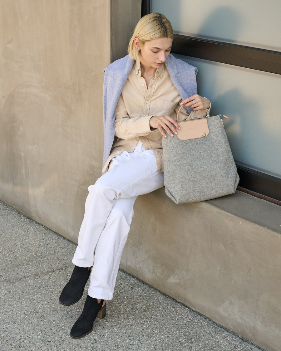 A Bedford Merino Wool Felt Backpack held by a sitting woman, showcasing its beige and grey colors