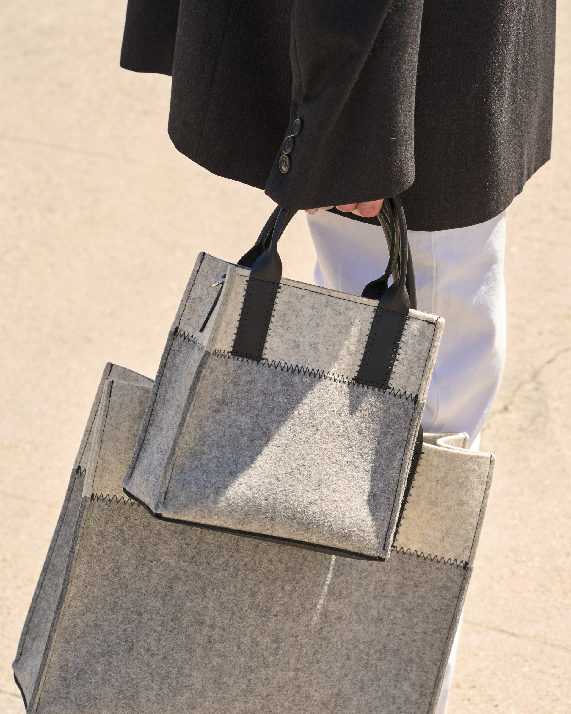 Two Jaunt Merino Wool Felt Tote bags in two different sizes in grey and white colors carried by a woman in one hand, side view 