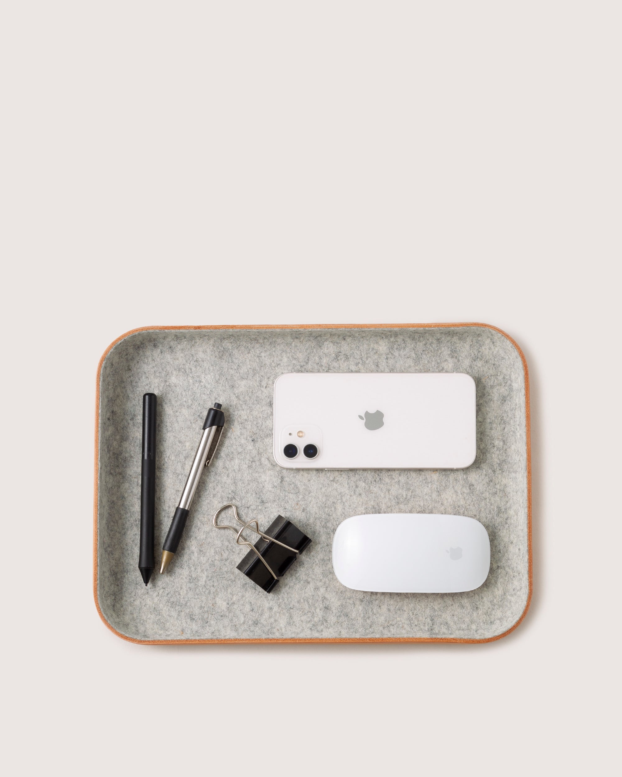 The neatly organized Kawabon Tray by graf lantz features a black pen, silver pen, two black binder clips, a white smartphone, and a white computer mouse. Crafted from Merino wool, this elegant tray sits gracefully against a light background.