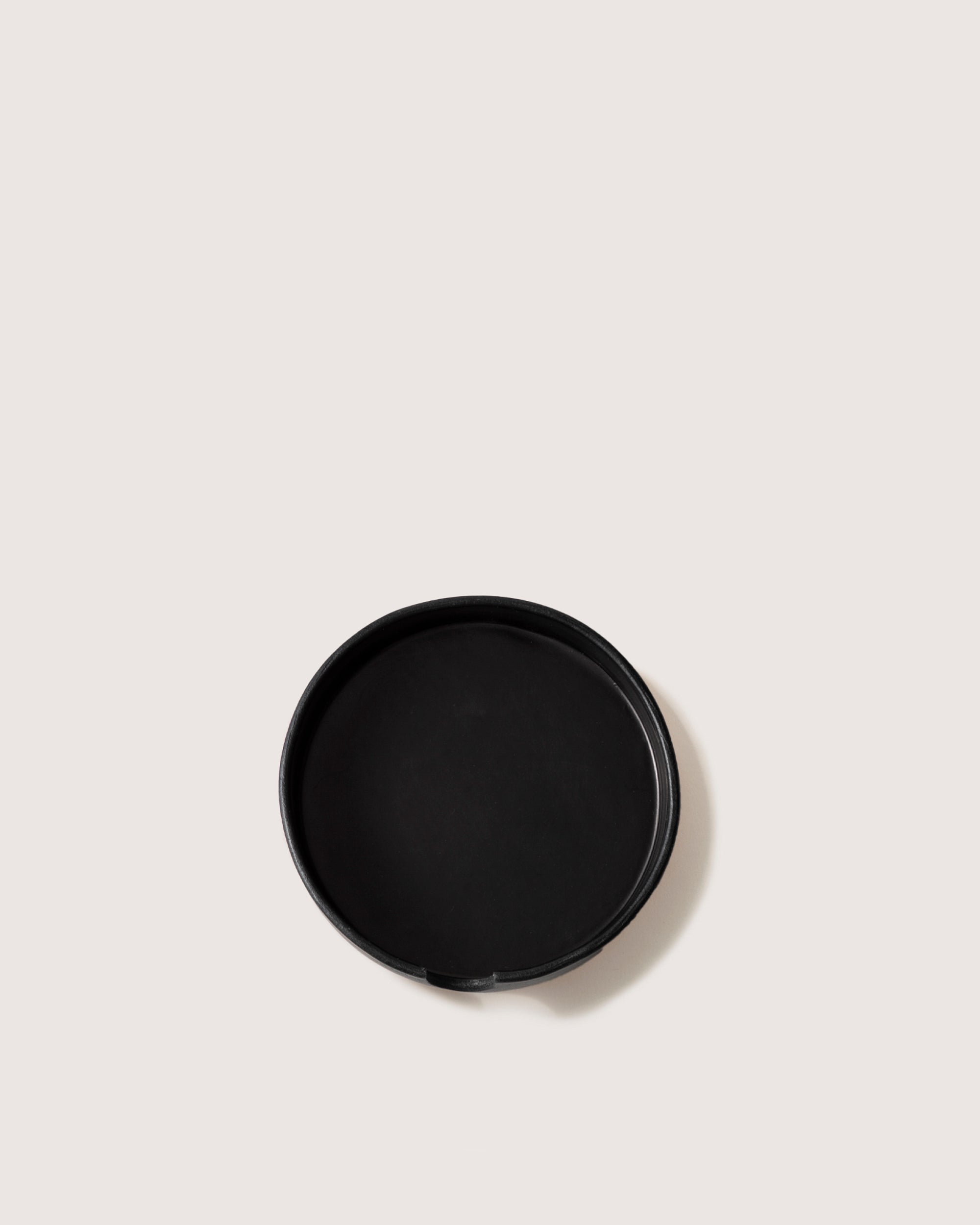 A round black baking pan by graf lantz rests on a light beige background, exuding minimalist elegance like a sculpted catch-all.