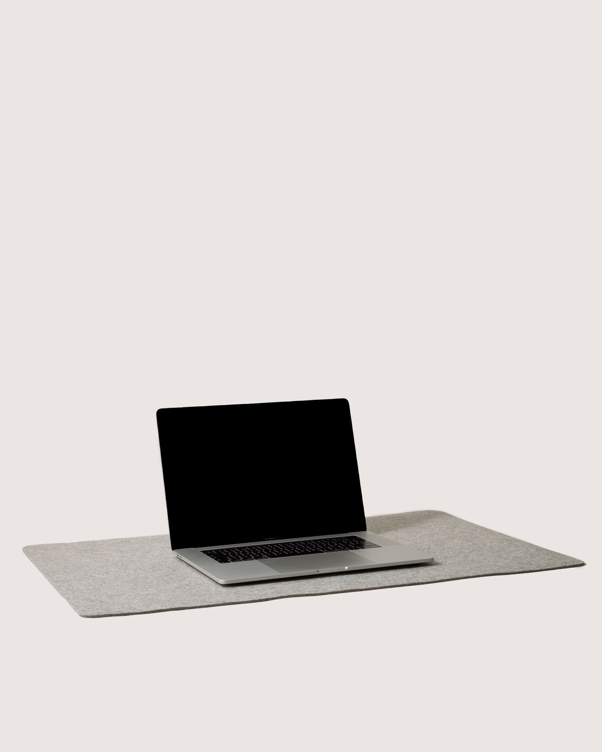 A laptop with a blank screen rests on a sleek graf lantz desk pad, enhancing the workspace against a plain white background.