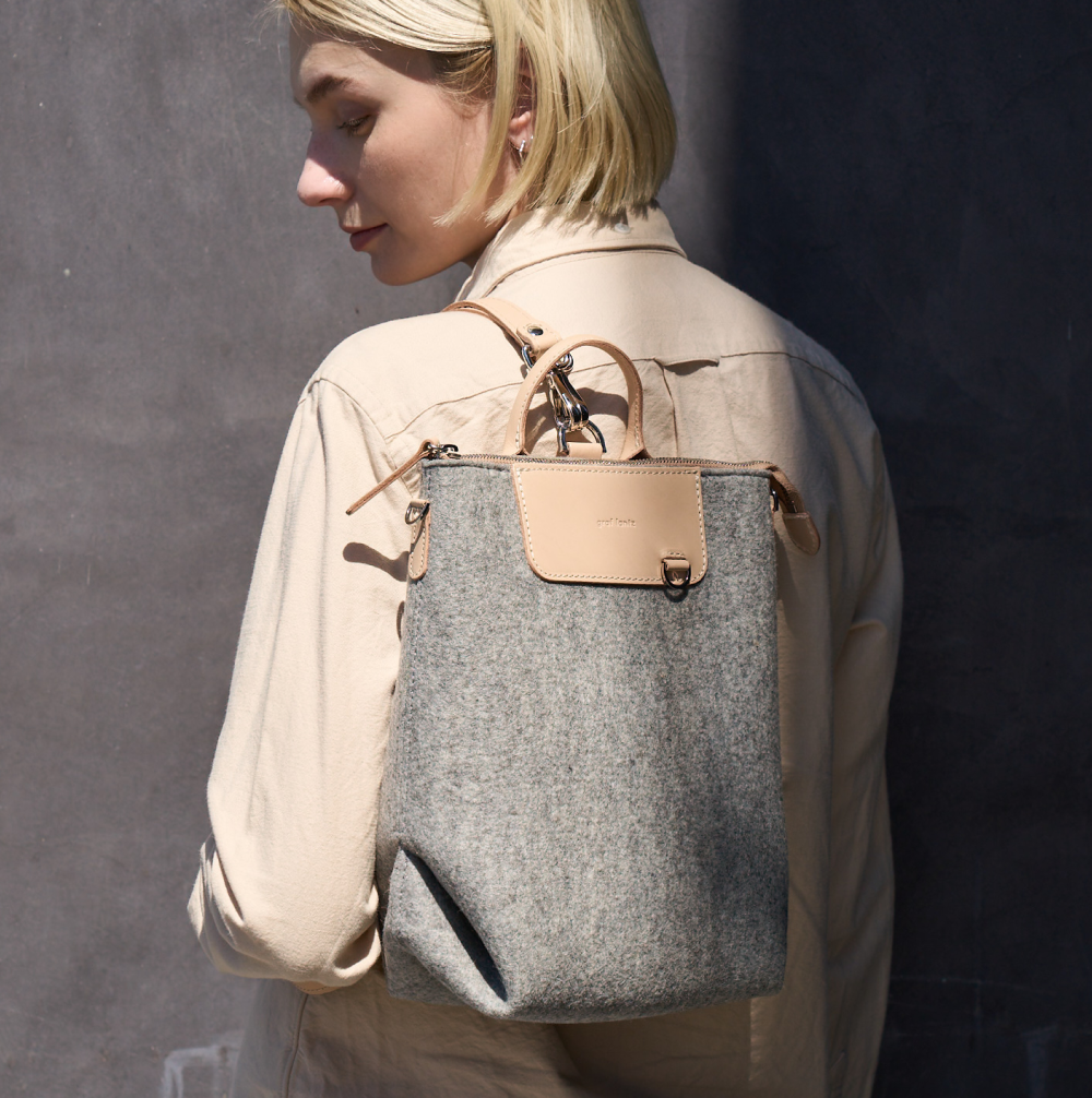 A Bedford Merino Wool Felt Belt Bag carried by a woman over her shoulder, showcasing its beige and light gray colors