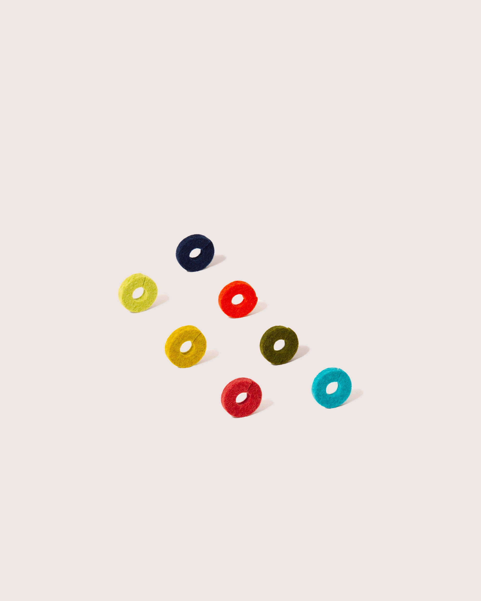 Graf Lantz presents eight vibrant, round candies resembling a playful set of wine markers, artistically arranged diagonally on a light beige background. Available in dark blue, yellow, black, red, green, and teal with right-cast shadows enhancing their 3D look—perfect for a unique host gift!.