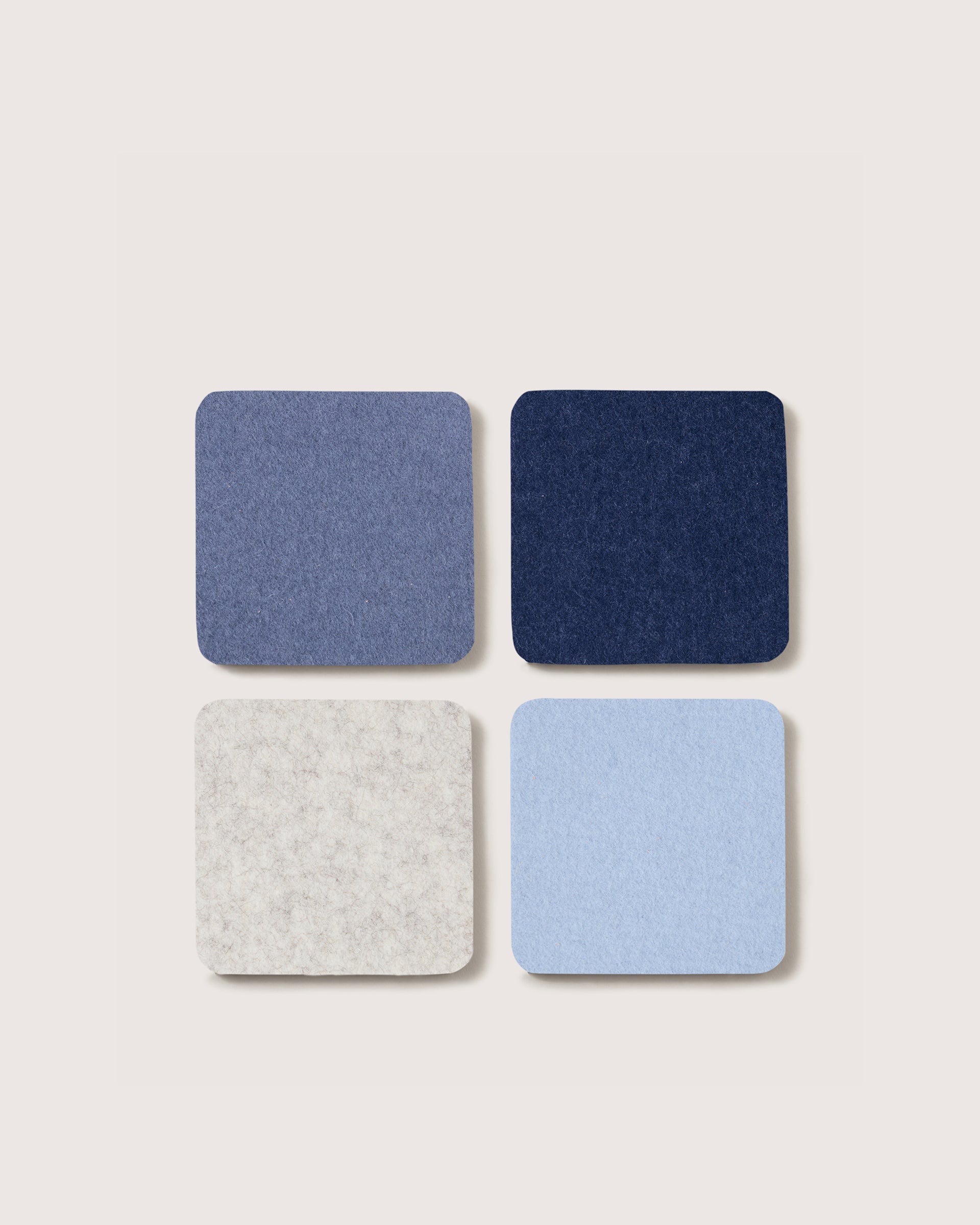Four square coasters in blue, gray, and light blue on a beige background
