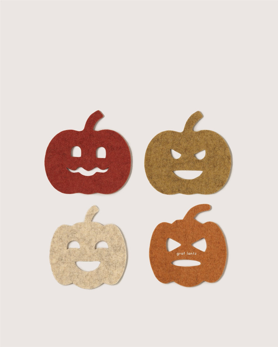 Four Graf Lantz felt coasters shaped like jack-o’-lanterns, each in red, brown, cream, or orange with unique faces, arranged in a grid on a light background.