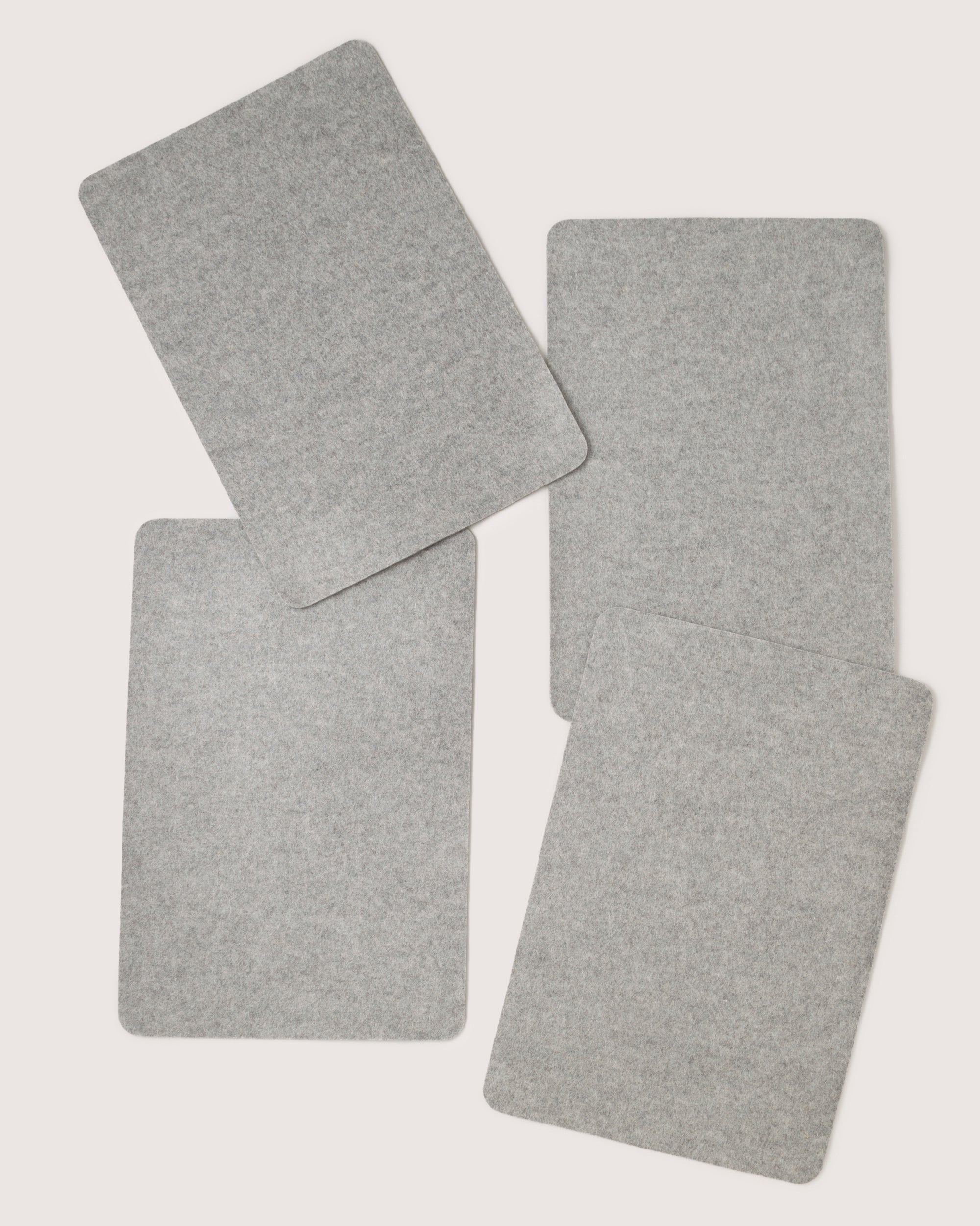 Four gray rectangular felt pads by graf lantz, crafted from premium Merino wool, are randomly arranged on a light background. Soft and slightly textured, they are similar in size and shape—ideal for a designer-inspired table setting.