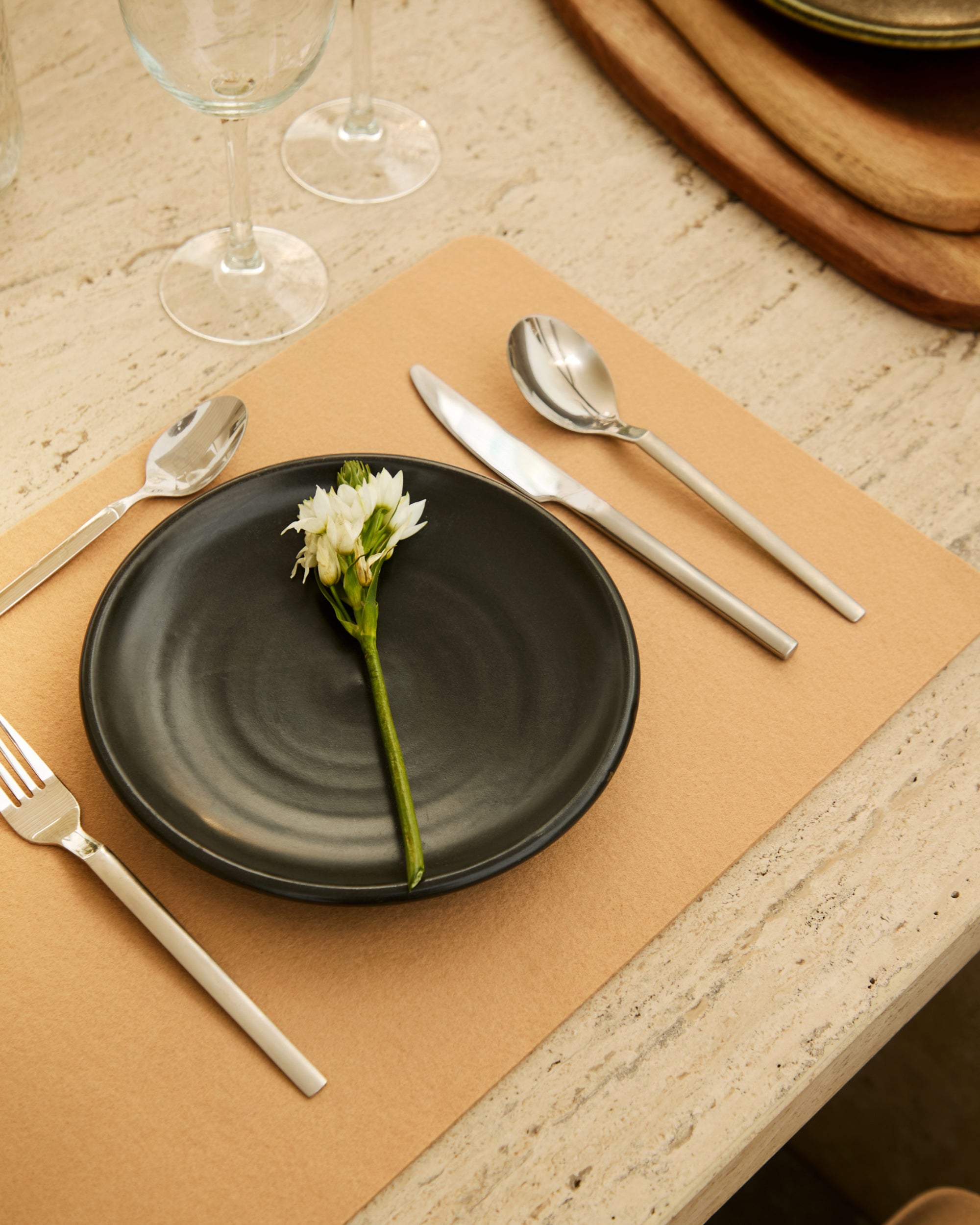 Dining table setting with black plate, silverware, and flower on a Latte placemat.