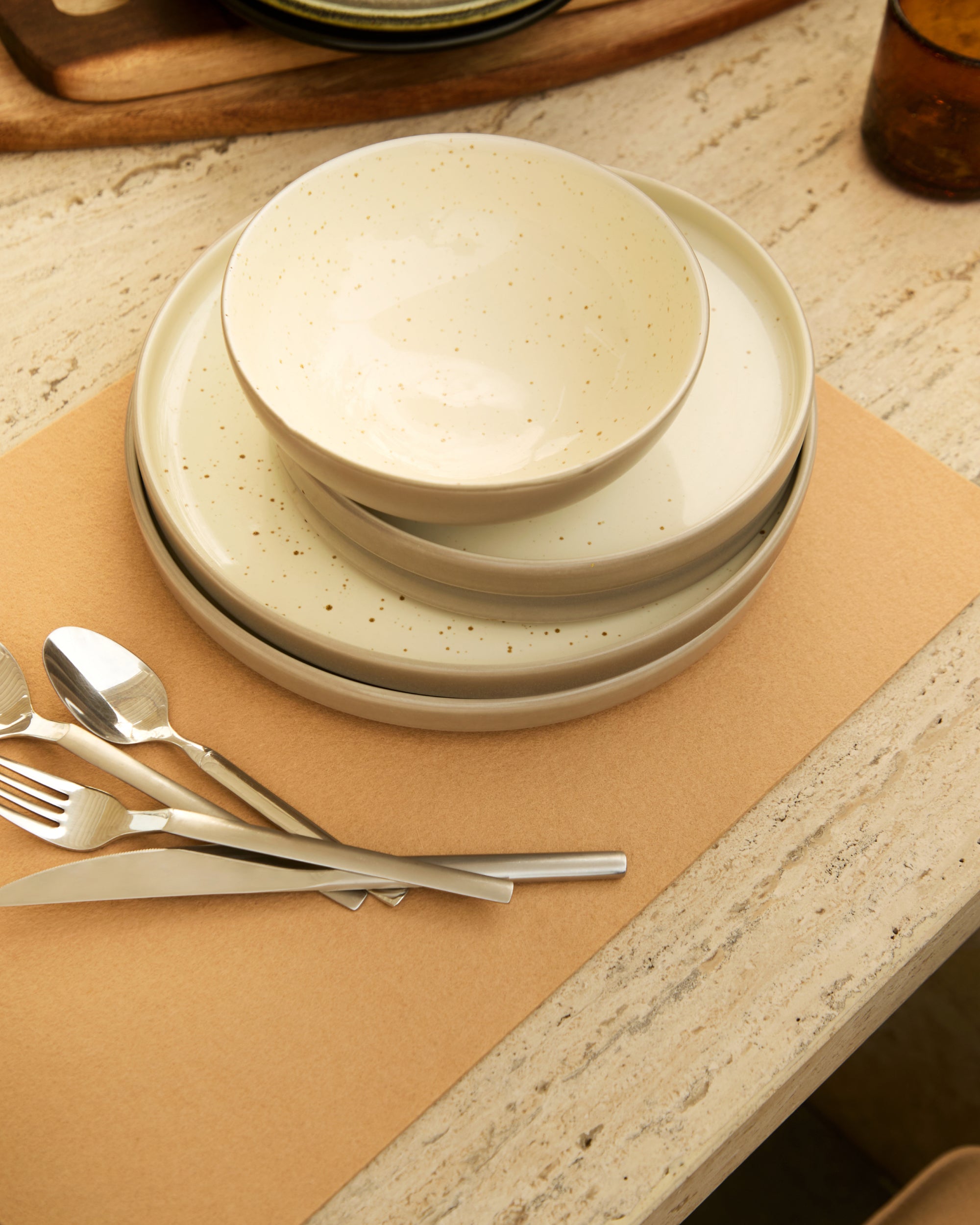 Stack of beige ceramic plates with silver cutlery on a brown placemat.