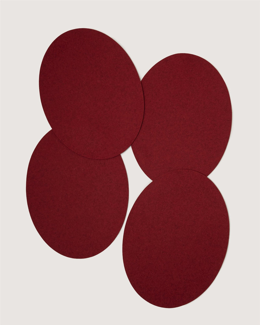 Four overlapping, round, dark red felt coasters by Graf Lantz are arranged on a plain white background.