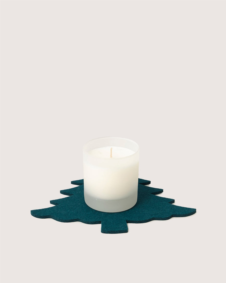 A white candle in a frosted glass holder from Graf Lantz sits on a dark green felt mat shaped like a Christmas tree, set against a plain light background.