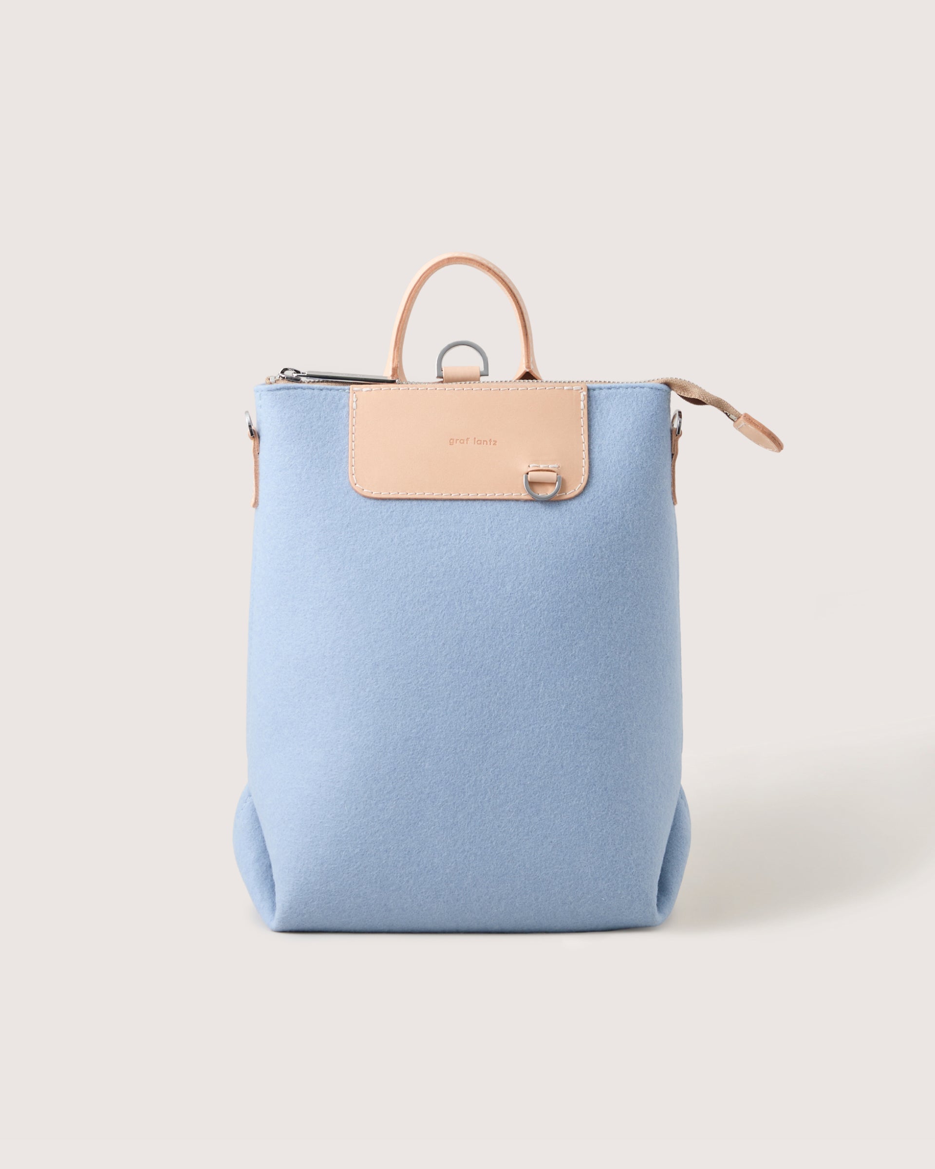 Light blue backpack with beige leather accents on a white background