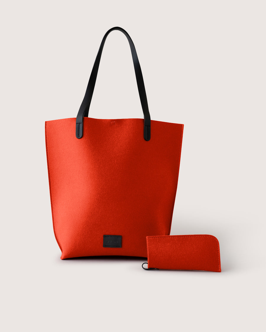 Orange Merino wool felt tote bag with black leather handle and matching eyeglass sleeve on a light gray background