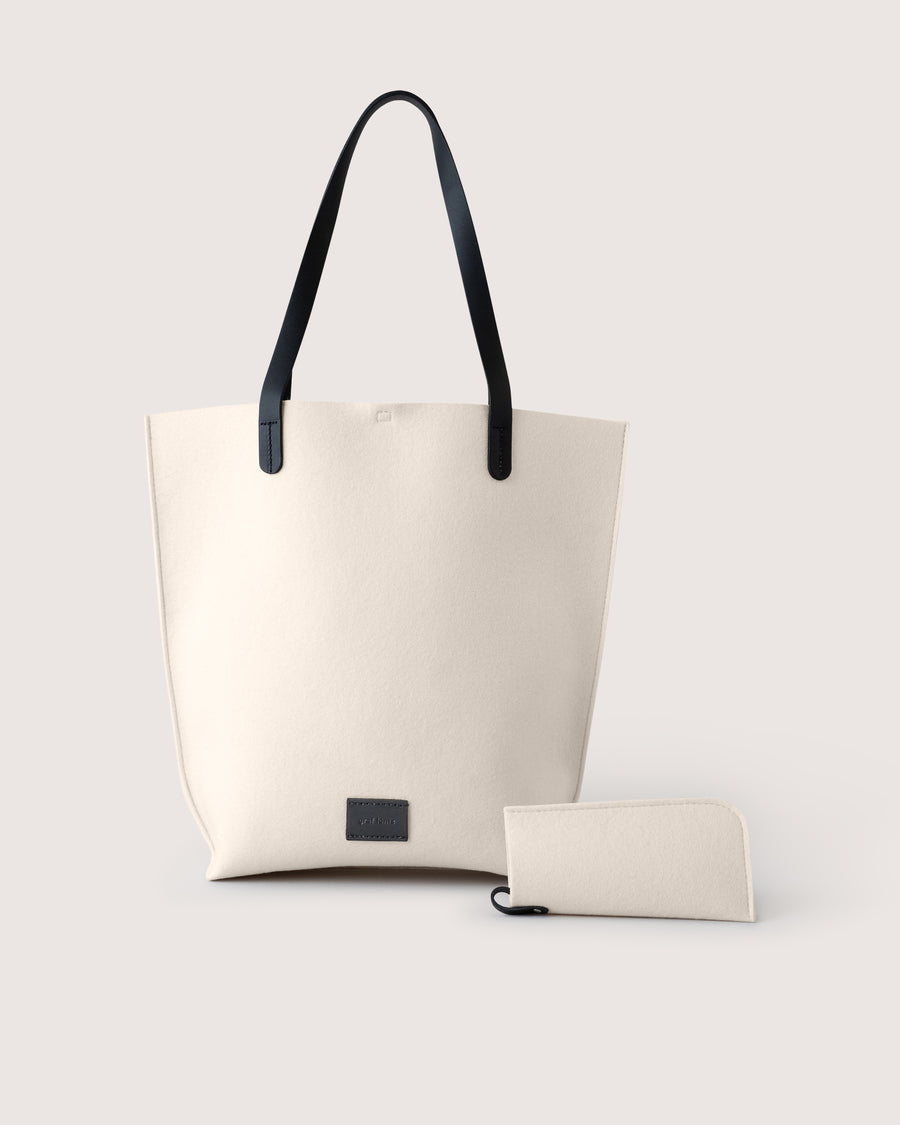 White Merino wool felt tote bag with black leather handle and matching Merino wool eyeglass sleeve on a light gray background