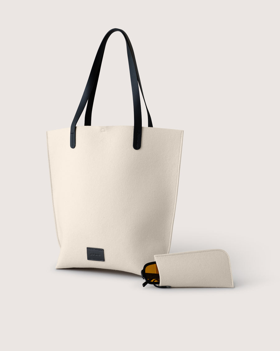 White Merino wool felt tote bag with black leather handles and a matching Merino wool eyeglass sleeve on a light gray background