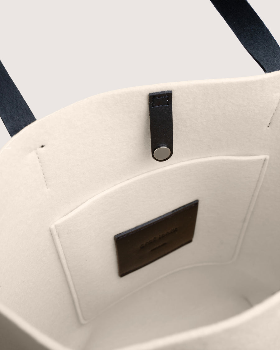 Close-up of a White Merino wool felt tote bag with black leather accents on a white background