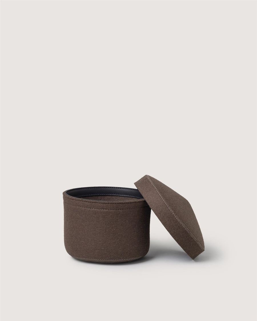 A round, brown fabric container by Graf Lantz with a matching lid set ajar beside it, displayed against a plain light background.