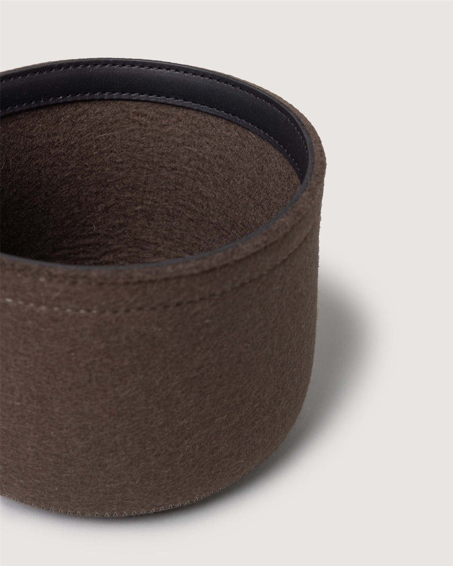 A close-up of a round, brown Graf Lantz felt container with a dark interior, set on a light, neutral background.