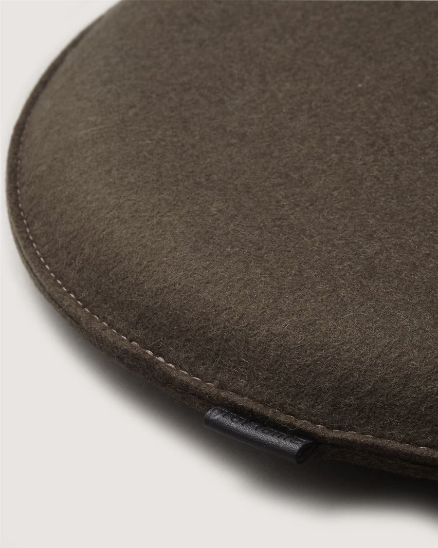 Close-up of a brown wool flat cap by Graf Lantz, highlighting its curved edge, detailed stitching, and a small black fabric tag.