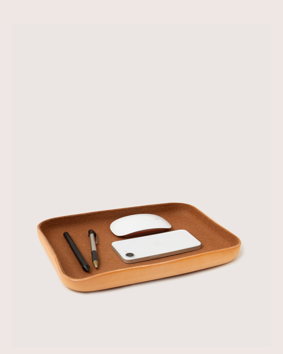 A graf lantz Kawabon Tray in tan leather neatly displays a white mouse, white smartphone, black pen, and mechanical pencil against a light background.