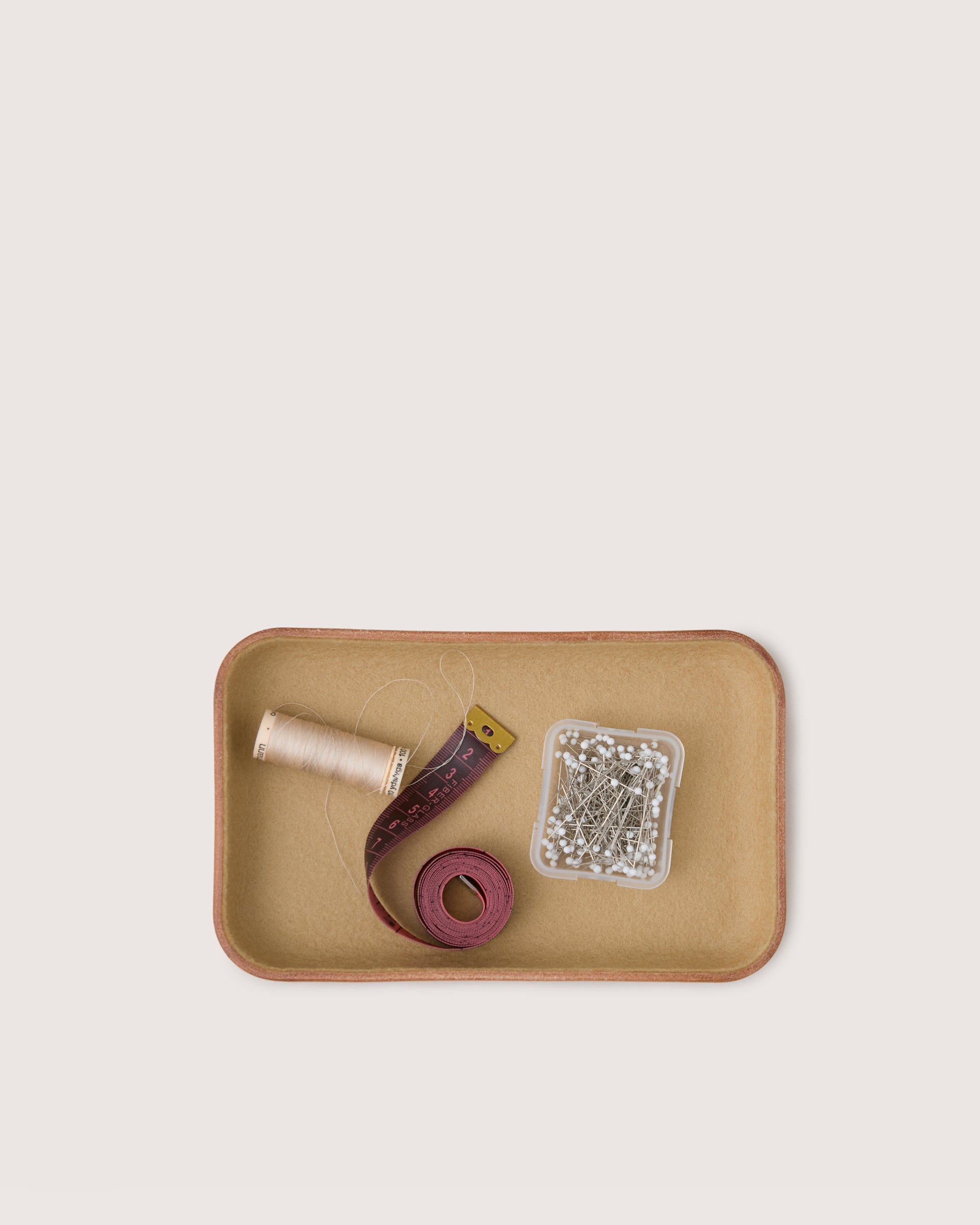 Tray with spool of thread, scissors, and decorative elements on a beige background