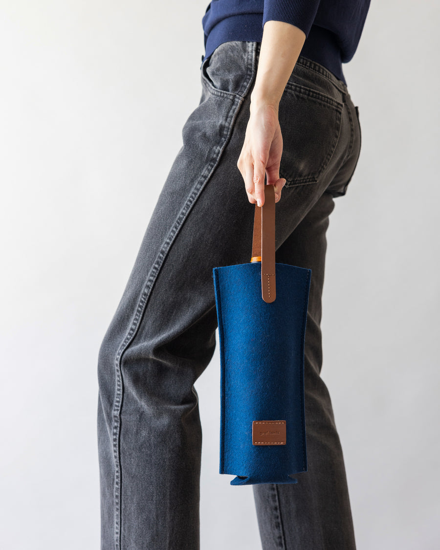A woman holding a Merino Wool Felt Single Wine Carrier in blue with a brown leather handle, side view