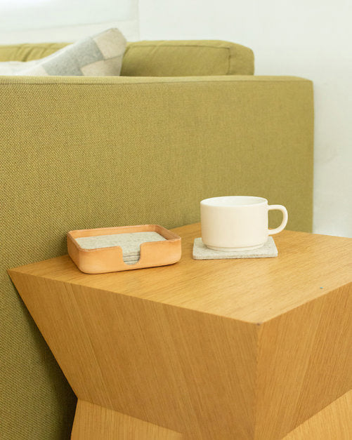 In front of green couch a wooden side table with bron coaster holder and grey square coaster by Graf Lantz