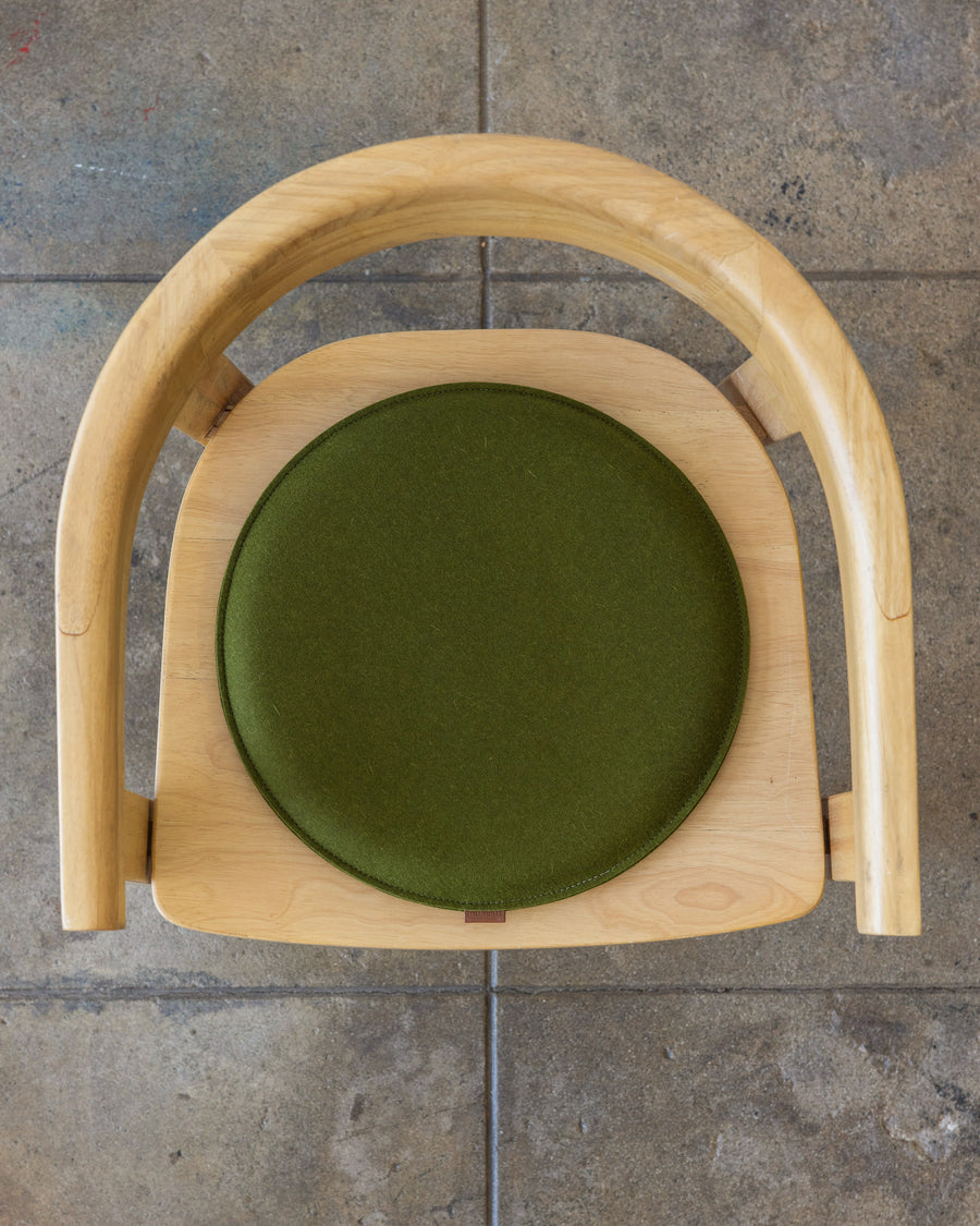A round Zabuton Merino Wool Felt Seat Pad by Graf Lantz in Moss Sienna on a wooden chair, view from above
