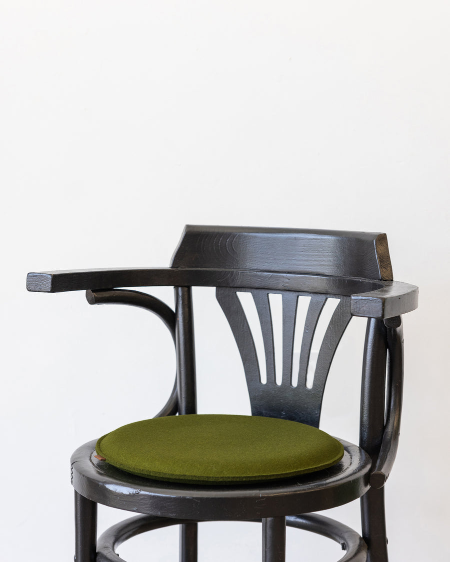 A round Zabuton Merino Wool Felt Seat Pad by Graf Lantz in Moss Sienna on a black chair, side view 