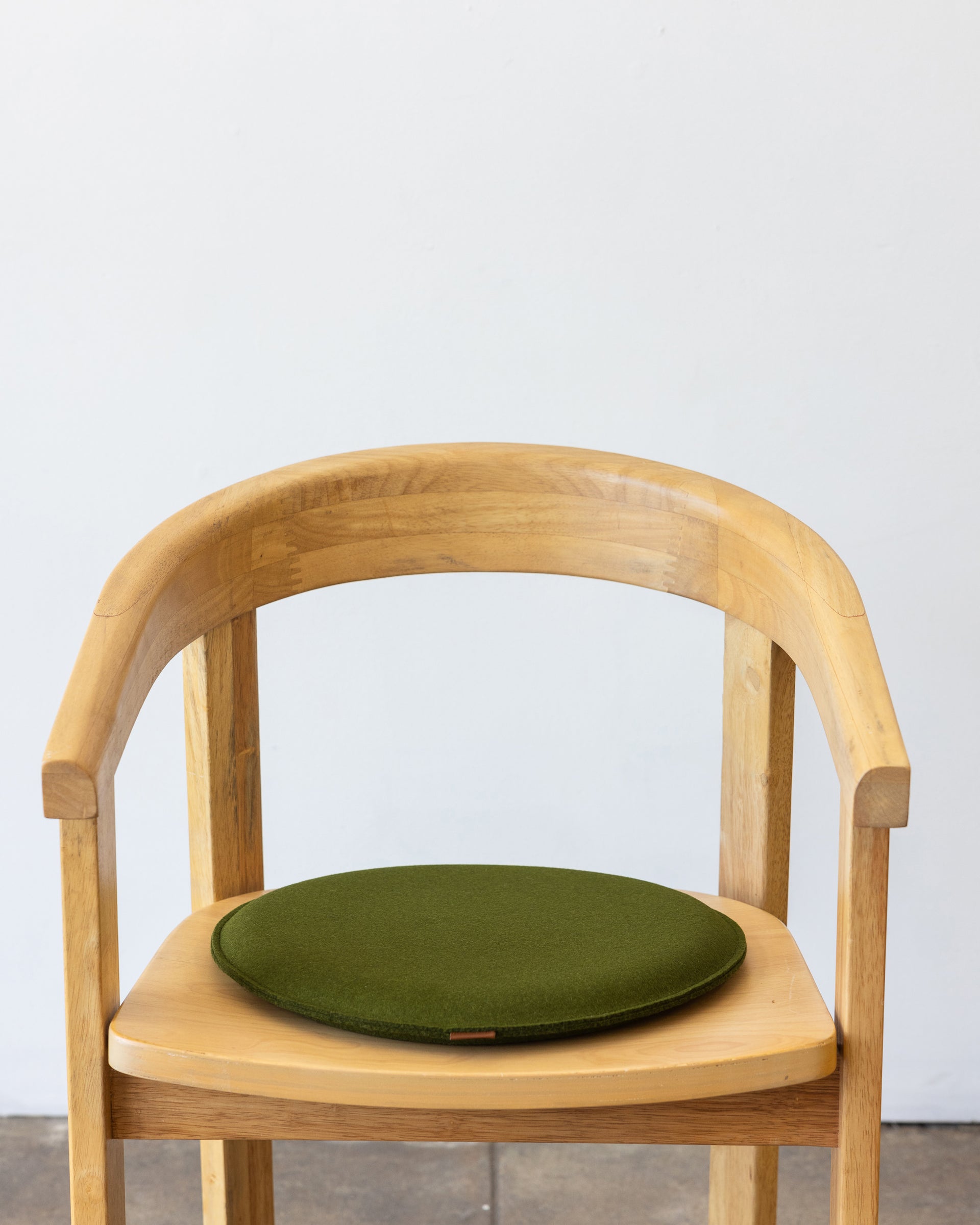 A green Zabuton Merino Wool Felt Round Seat Pad by Graf Lantz on a wooden chair, front view