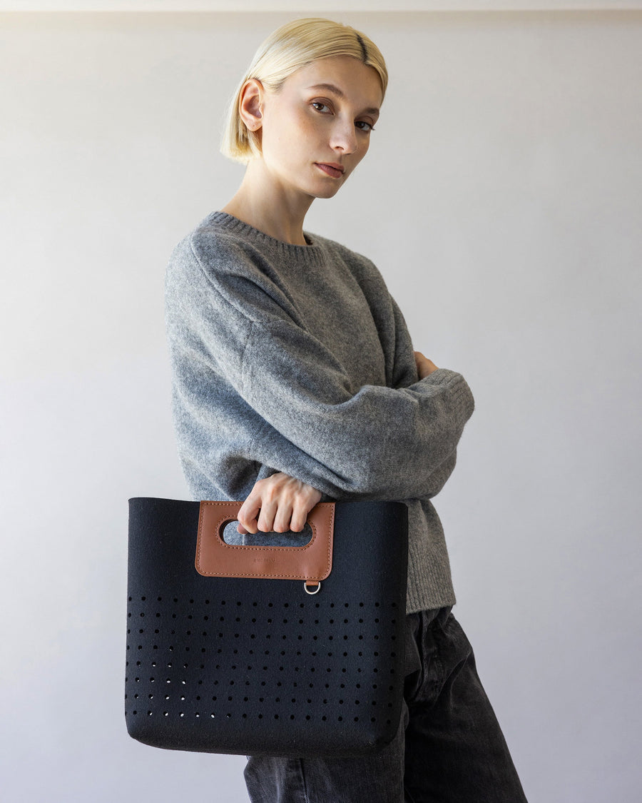 Woman with crossed arms holds black Asobi Merino Wool Midi in one hand, side view