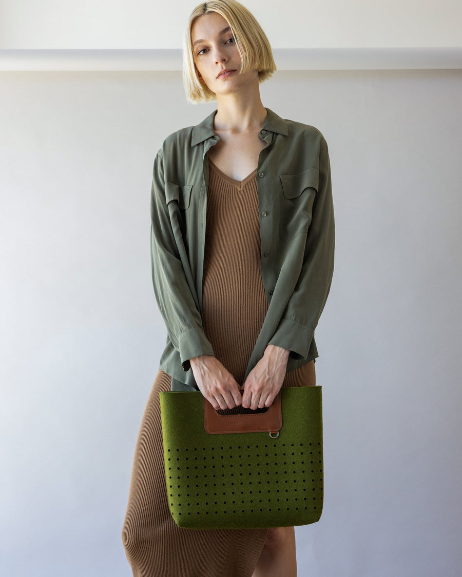 Standing woman holds green Asobi Merino Wool Midi by Graf Lantz with both hands in front of her, front view