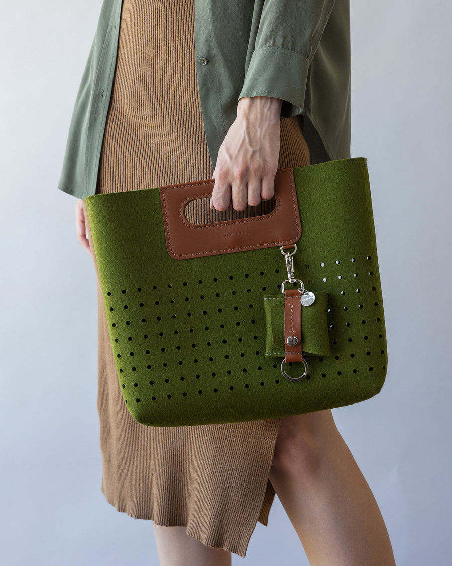 Standing woman with green Asobi Merino Wool Midi with color matching Merino Wool Pod Key Fob in one hand, side view