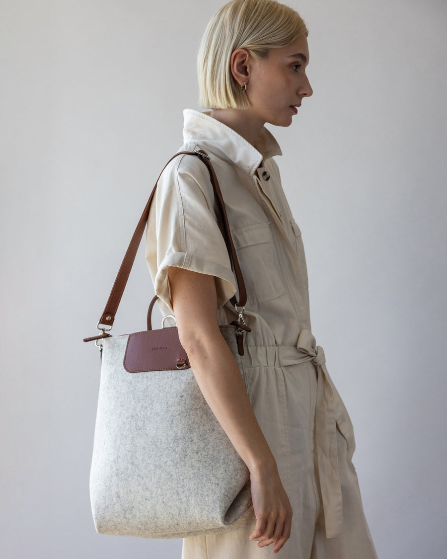 Standing woman with brown leather bag strap of white Bedford Merino Wool Backpack over one shoulder, side view