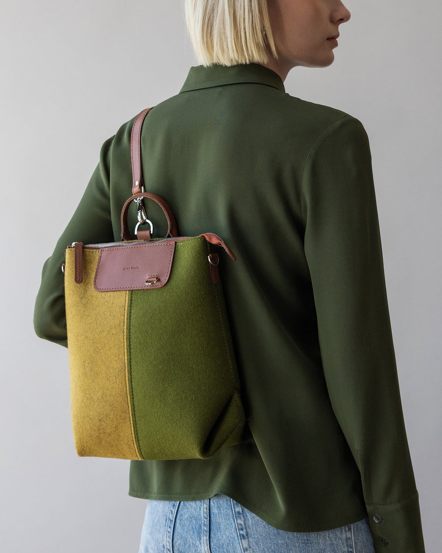 Standing woman with Bedford Merino Wool Colorblock Midi Backpack in Moss and Ochre over one shoulder, rear view