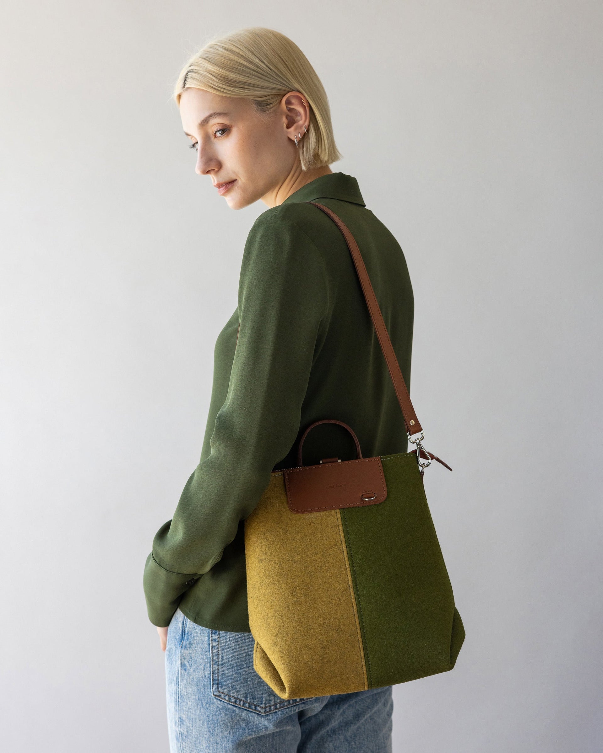 Standing woman with bag strap of Bedford Merino Wool Colorblock Midi Backpack in Moss and Ochre over one shoulder, side view