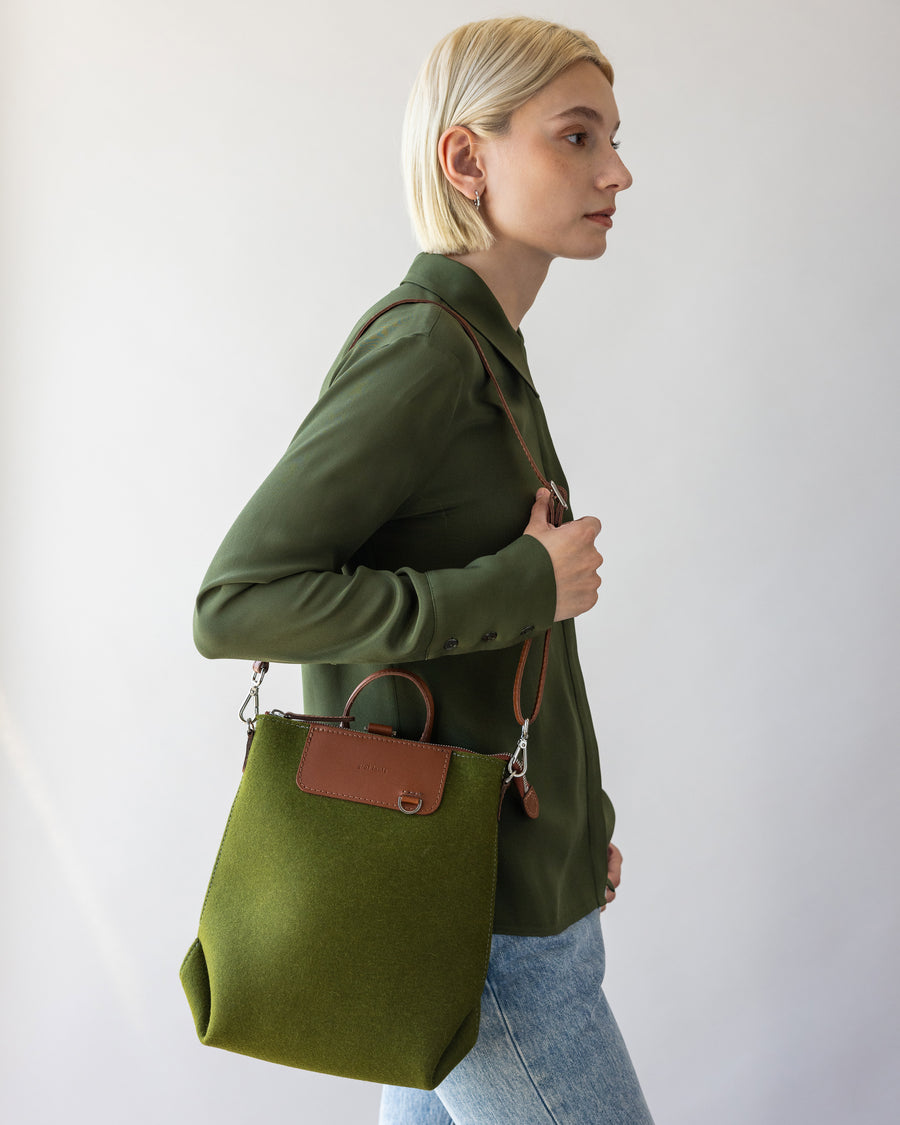 Walking woman with brown leather bag strap of green Bedford Merino Wool Midi Back one shoulder, side view