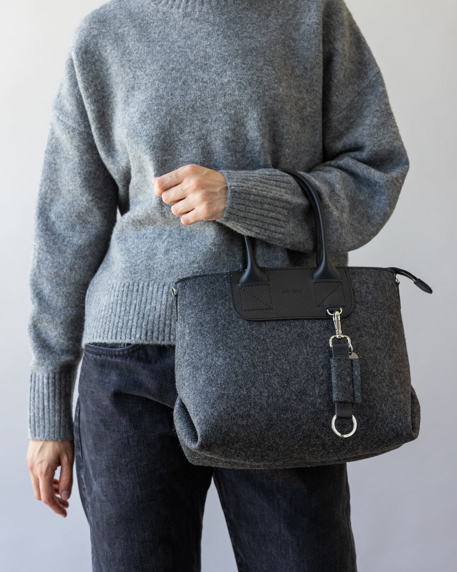 Standing woman with handles of charcoal Bedford Merino Wool Stachel over one arm, front view