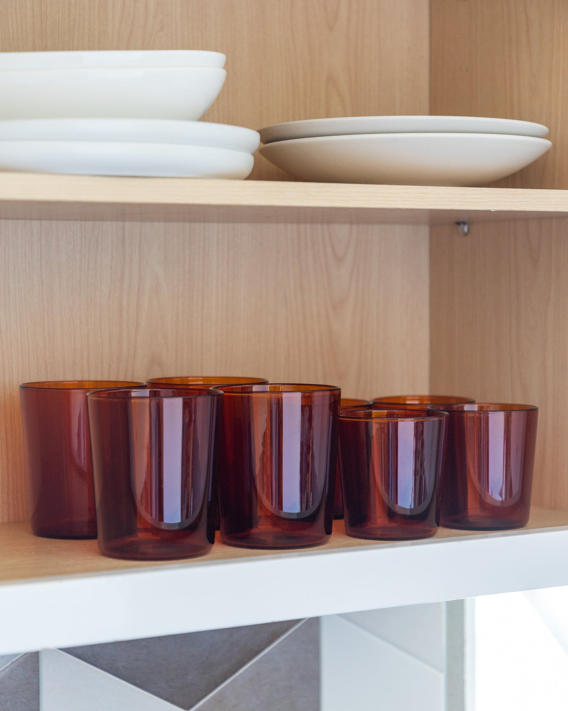 View inside a kitchen cabinet with different sized drinking glasses in color burnt orange