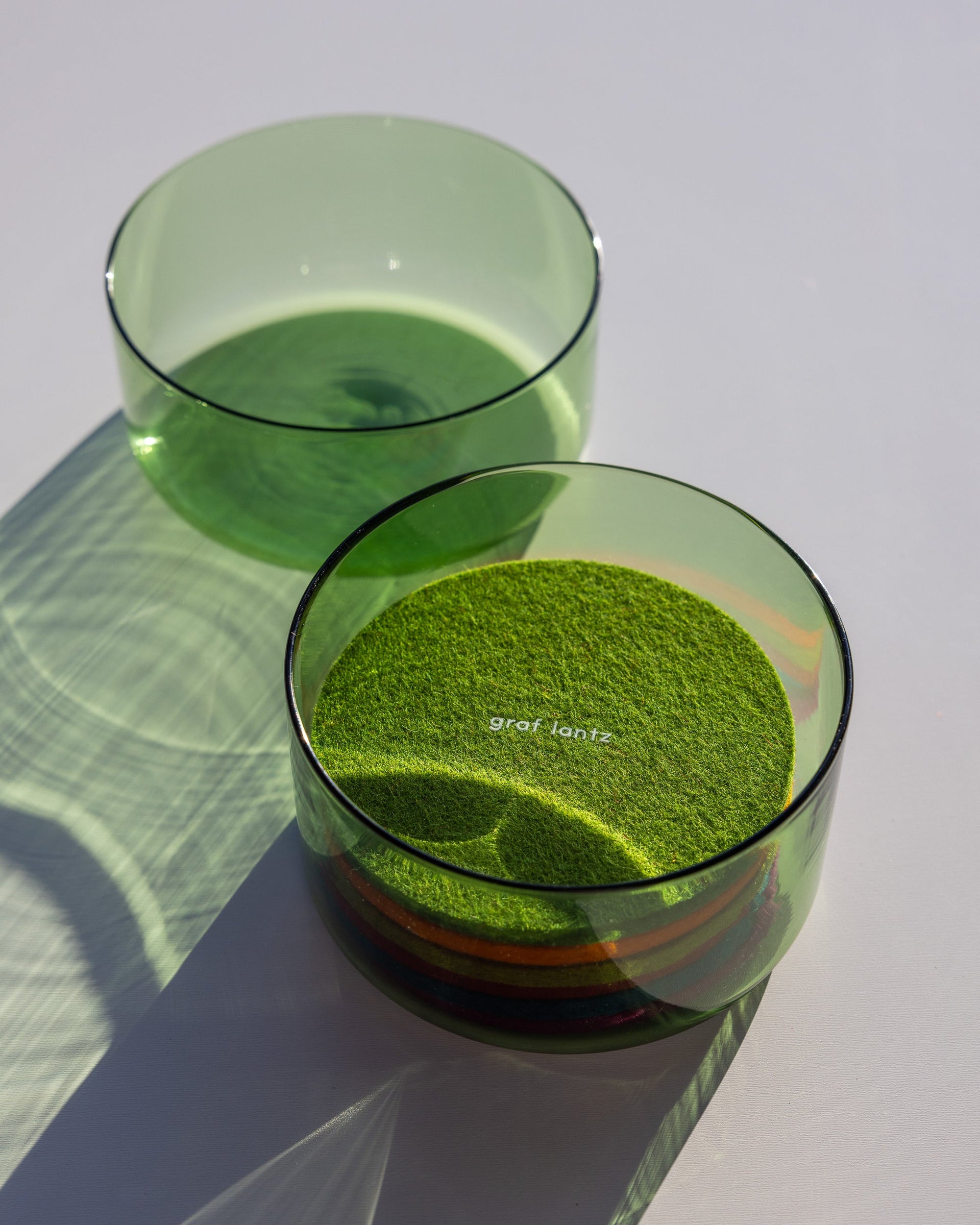 Cactus colored glass lid next to small class container with round coasters inside, white background