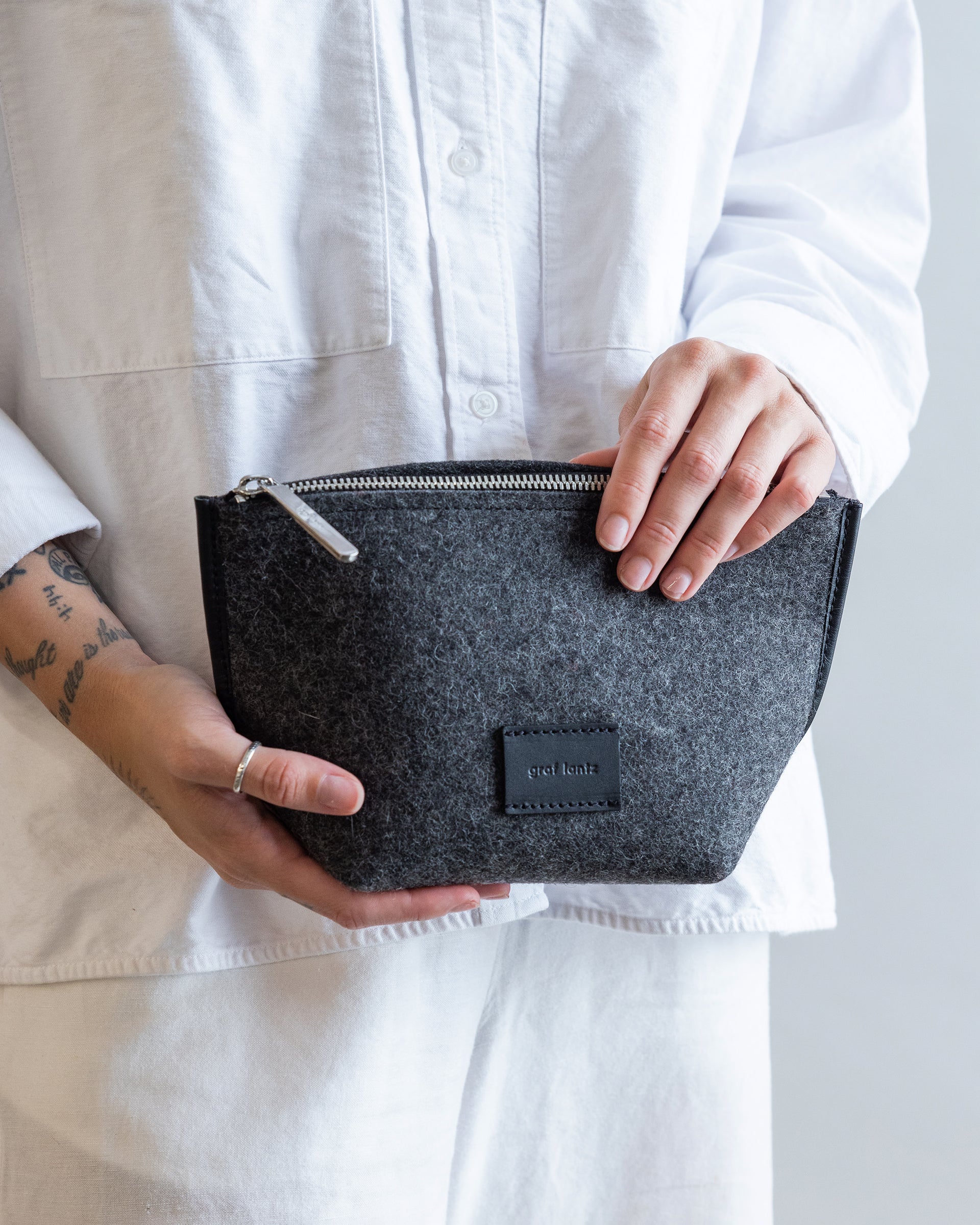 Standing woman holding Hana Merino Wool Pouch in charcoal by Graf Lantz in both hands in front of her