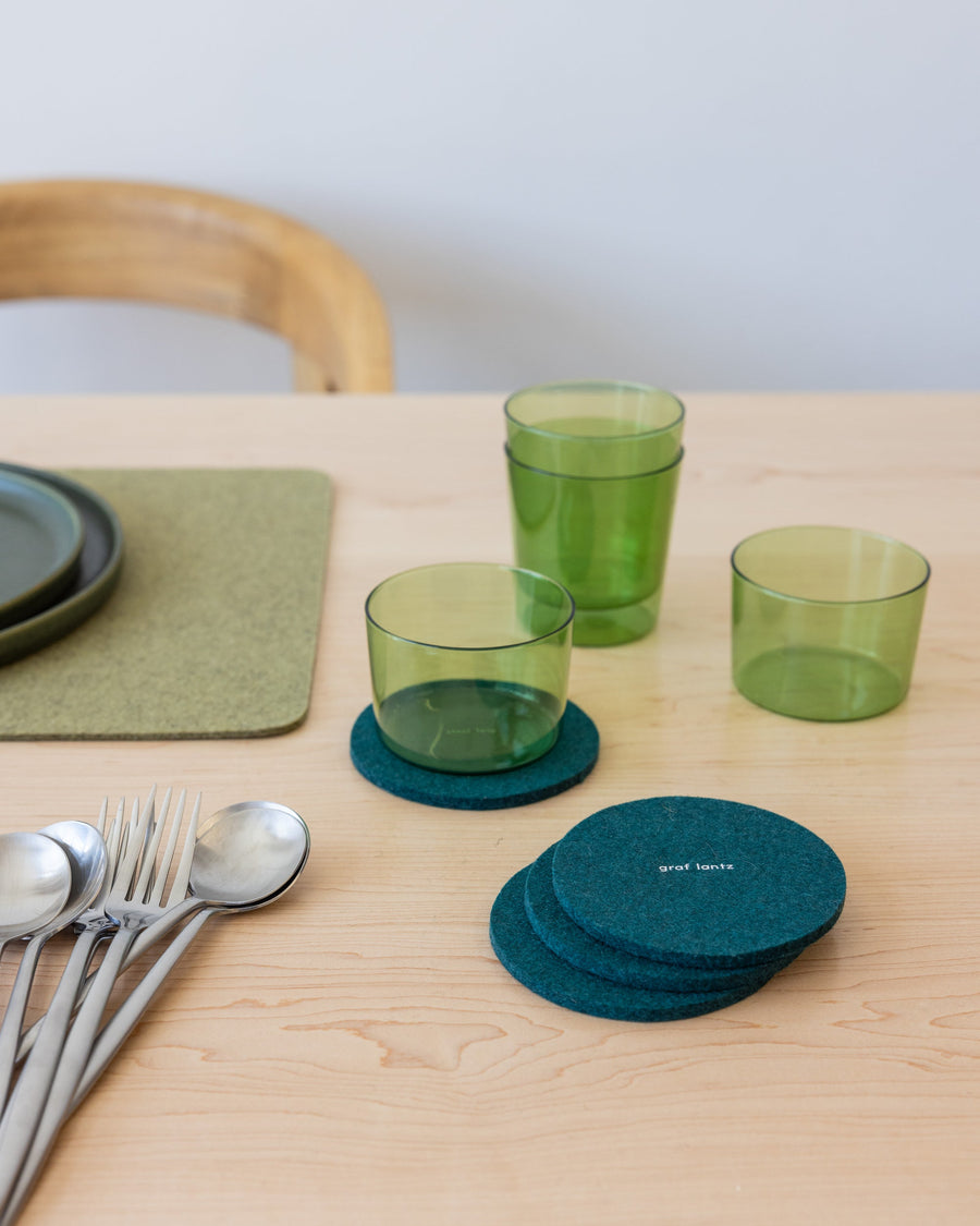 Table setting with green placemat, silver cutlery and round Kombu-colored coasters and green glasses