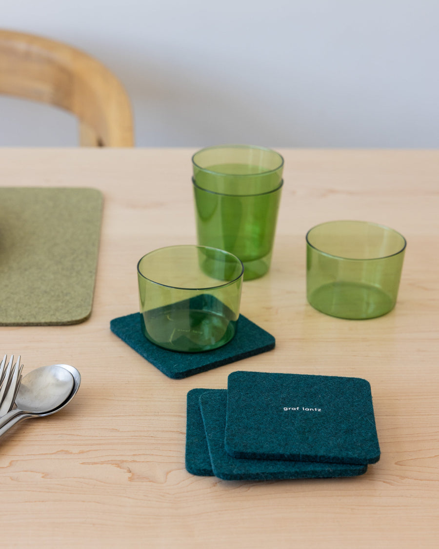 Table setting with green placemat, silver cutlery and square Kombu-colored coasters and green glasses