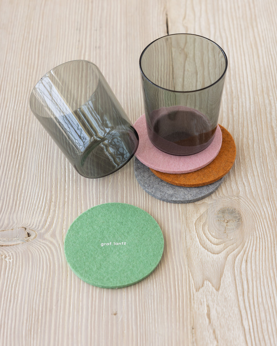 Four round coasters by Graf Lantz in four colors on a wooden tabletop, two black glasses