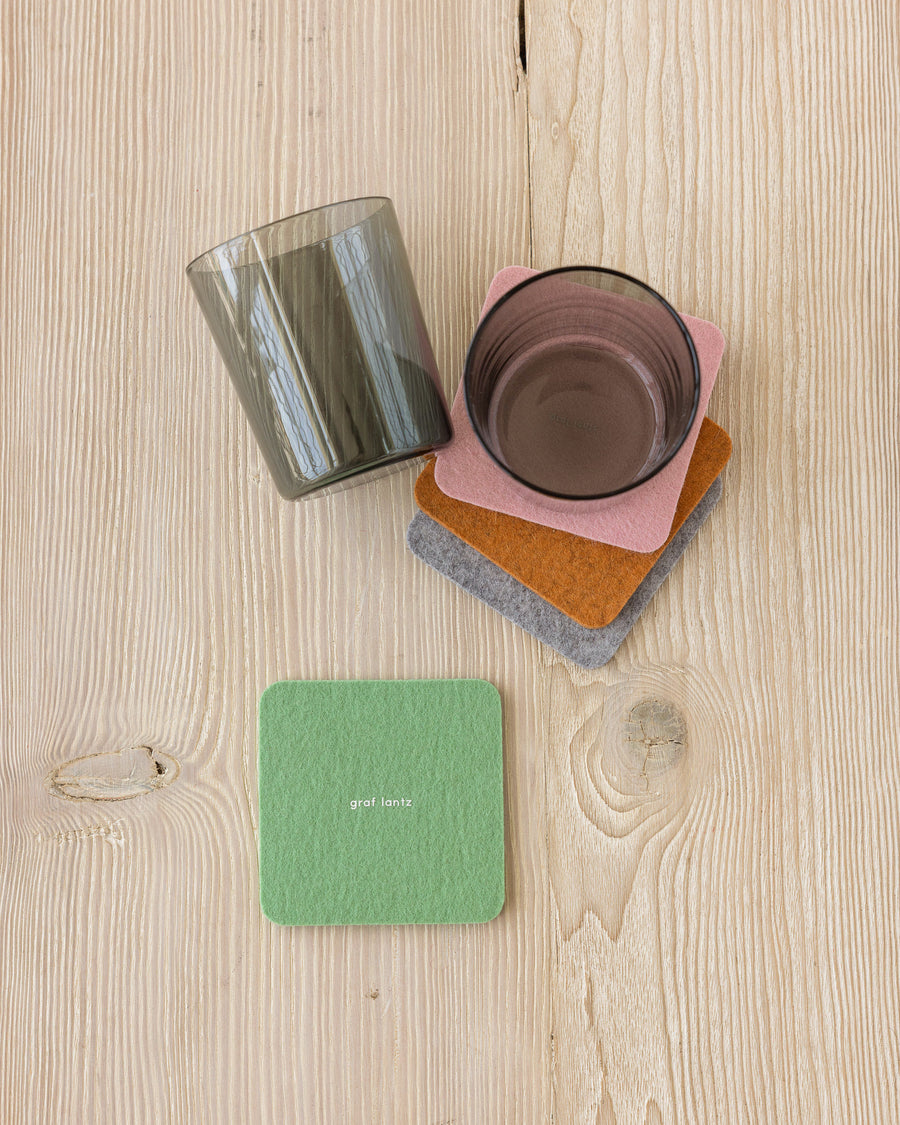 Stack of three square felt coasters in different colors under a black glass next to a green coaster and another black glass, view from above