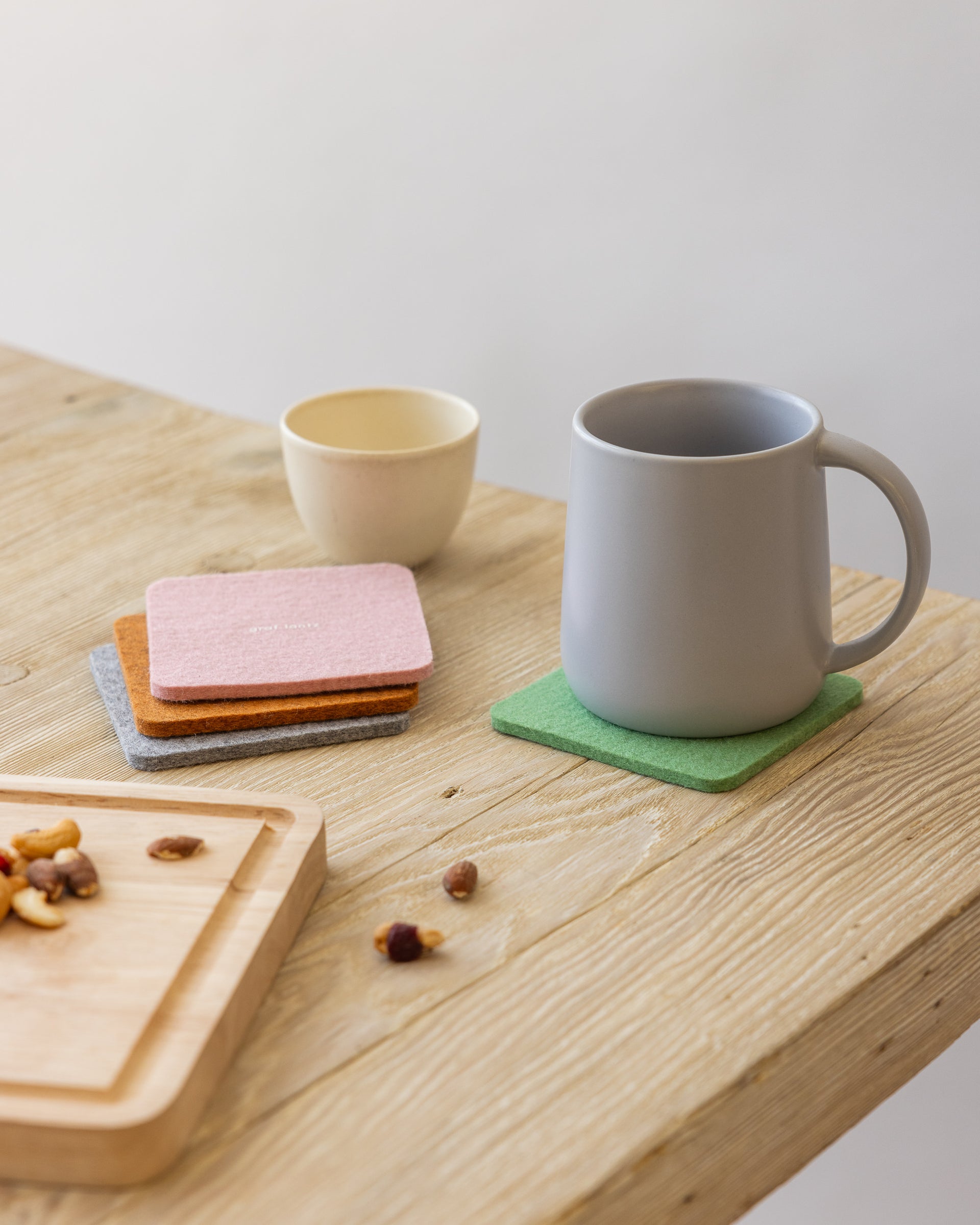 Stack of three square felt coasters, a white mug standing on a green coaster on a wooden tabletop