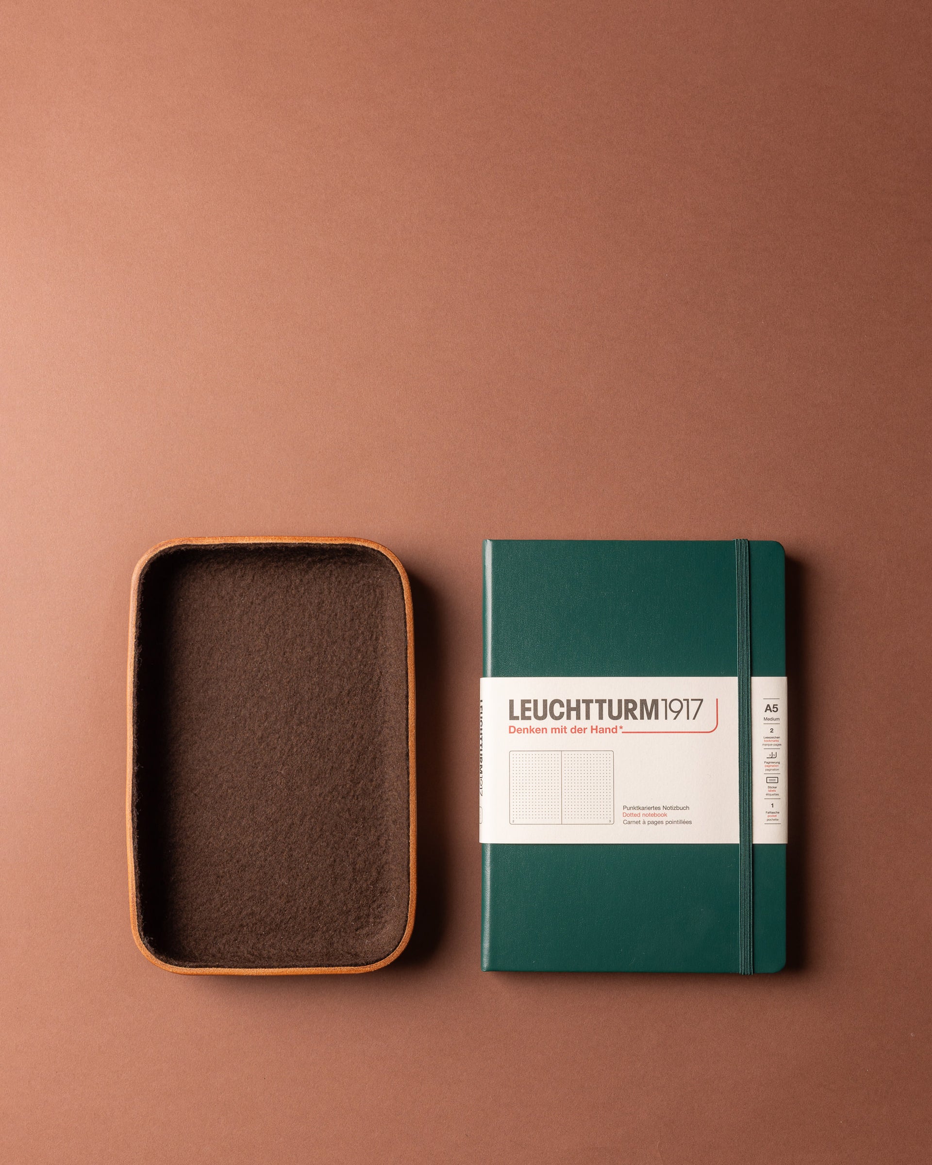 A green Graf Lantz notebook with a white label and a brown workspace organizer box.