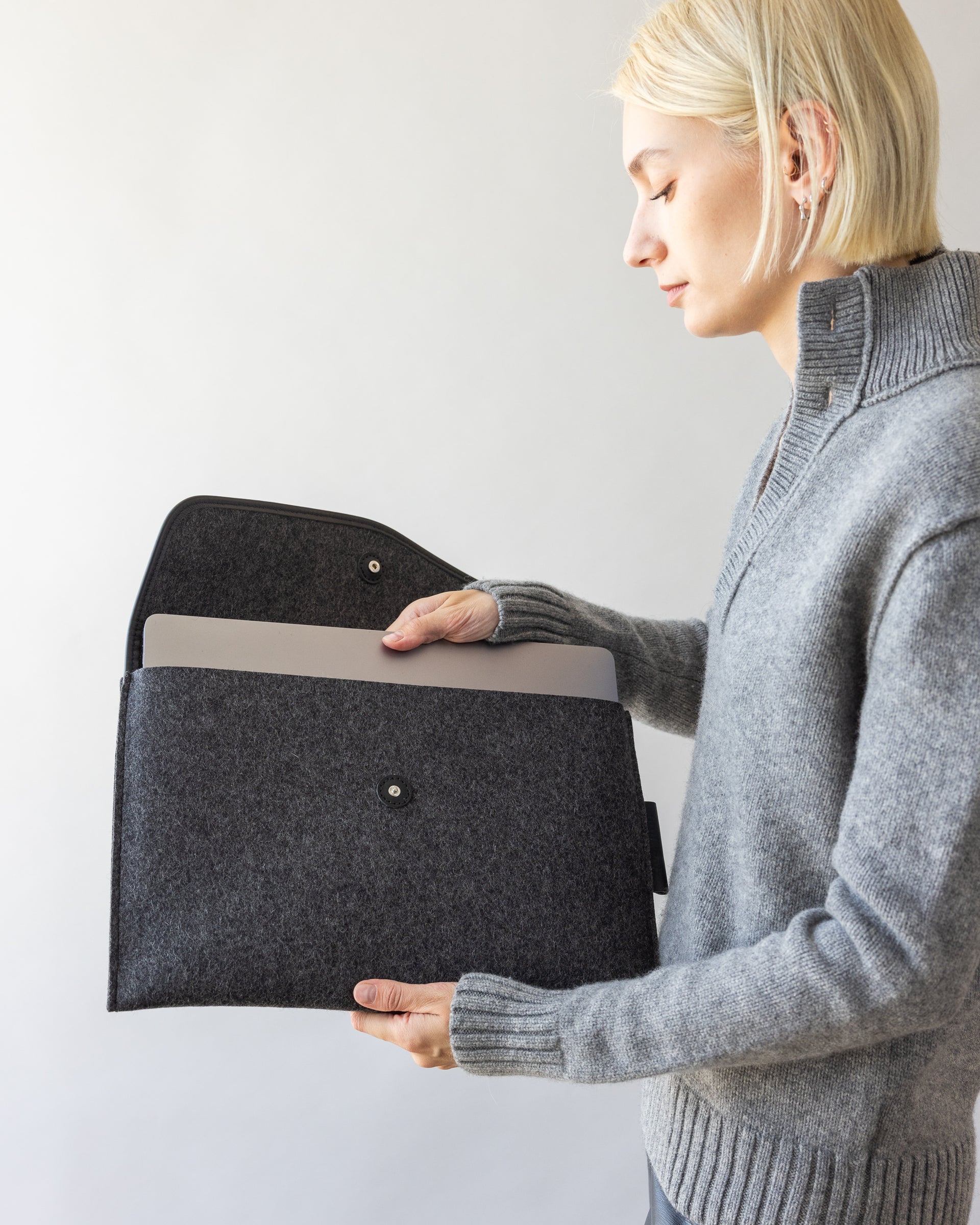 Stylish woman is pulling a silver colored laptop out of Envelope Merino Wool 16" Tech Sleeve in charcoal