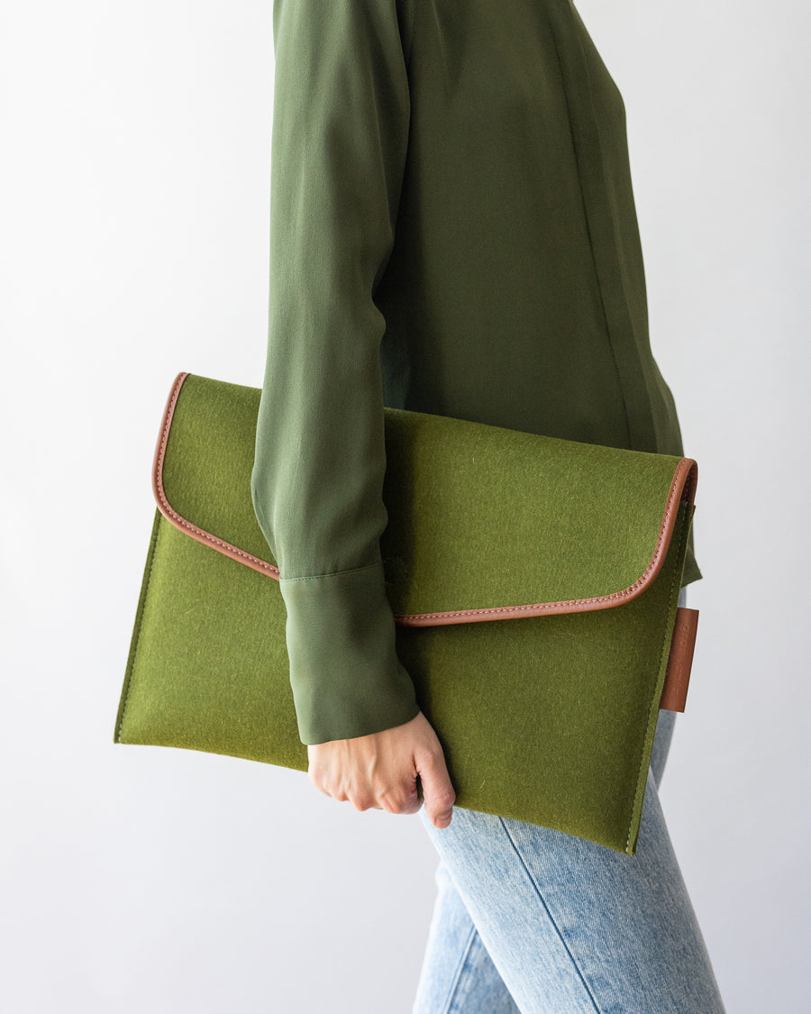 Envelope Merino Wool 16" Tech Sleeve in moss color held in one hand by a stylish woman, side view